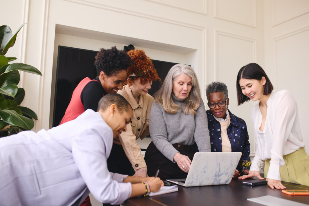 Portrait of multiethnic businesswomen looking at laptop on boardroom meeting table and discussing
